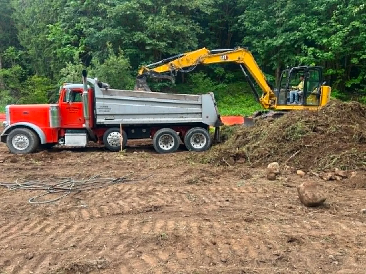 The Gritworks dump truck being loaded by an excavator on a cleared lot.