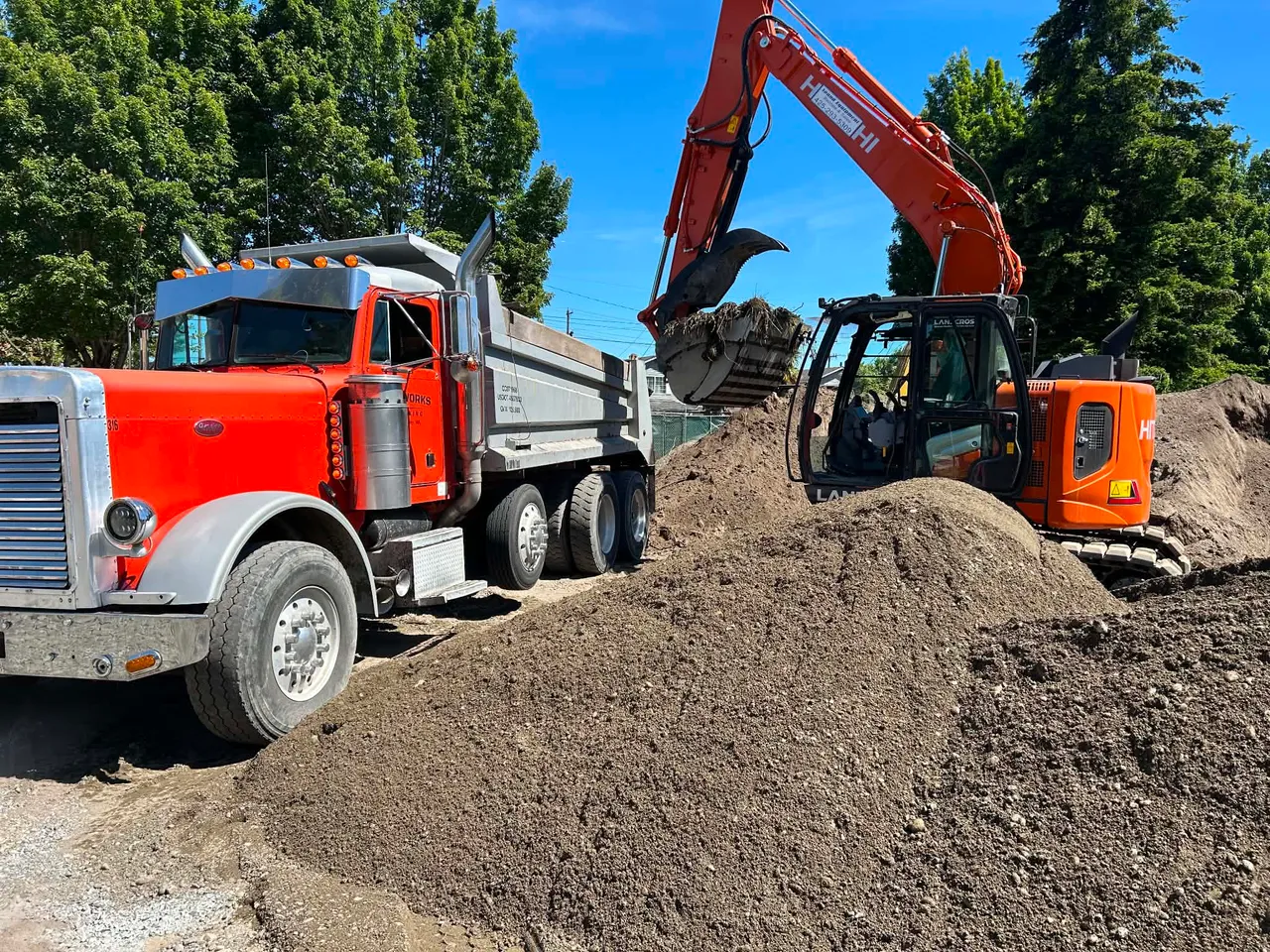 A Gritworks dump truck being loaded with soil by an excavator on a King County job site.